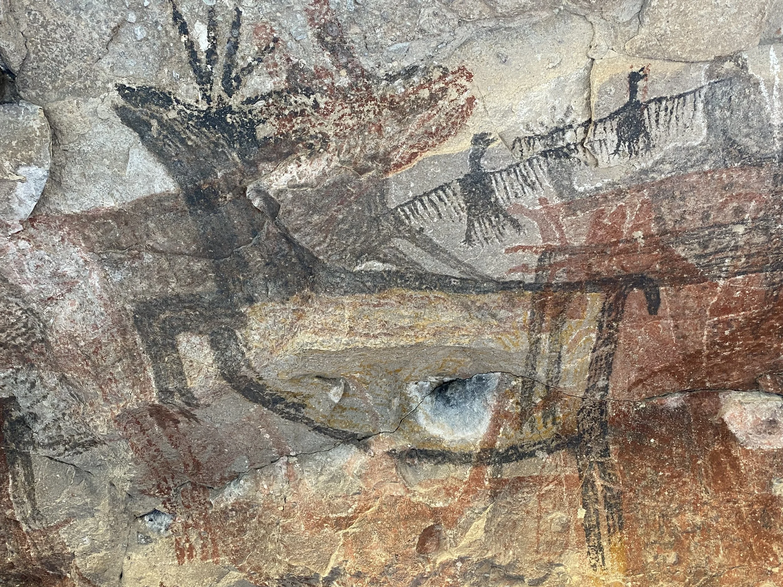 Prehistoric cave painting depicting a large bird, possibly an eagle, with outstretched wings and a human figure holding a spear, along with other animal figures on a rock wall.