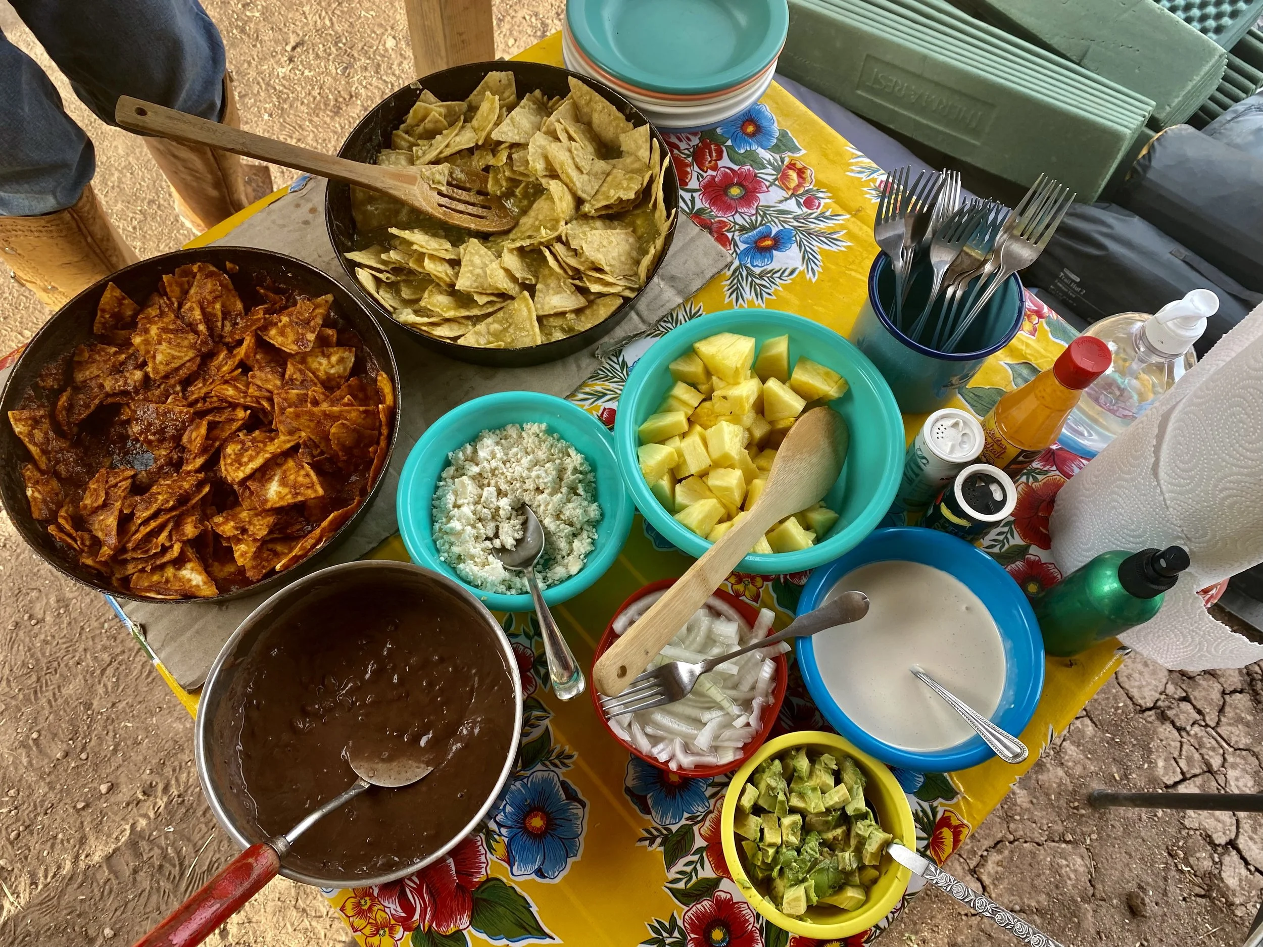 A table set with various bowls of Mexican food including chips, dip, salsa, avocado, and sauces, with utensils and paper towels.