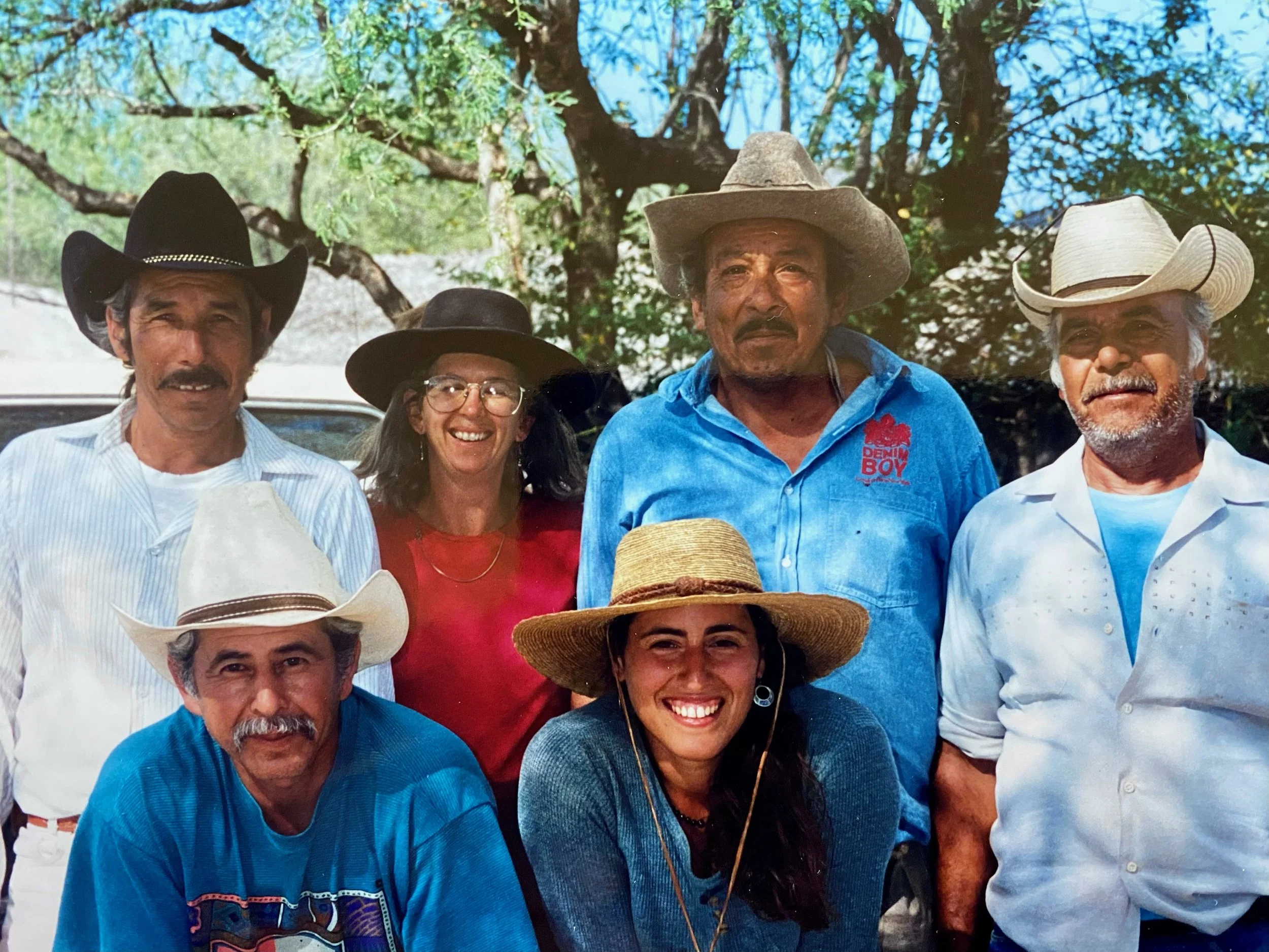 Group of six people, five men and one woman, wearing cowboy hats outdoors, smiling and posing for the photo.