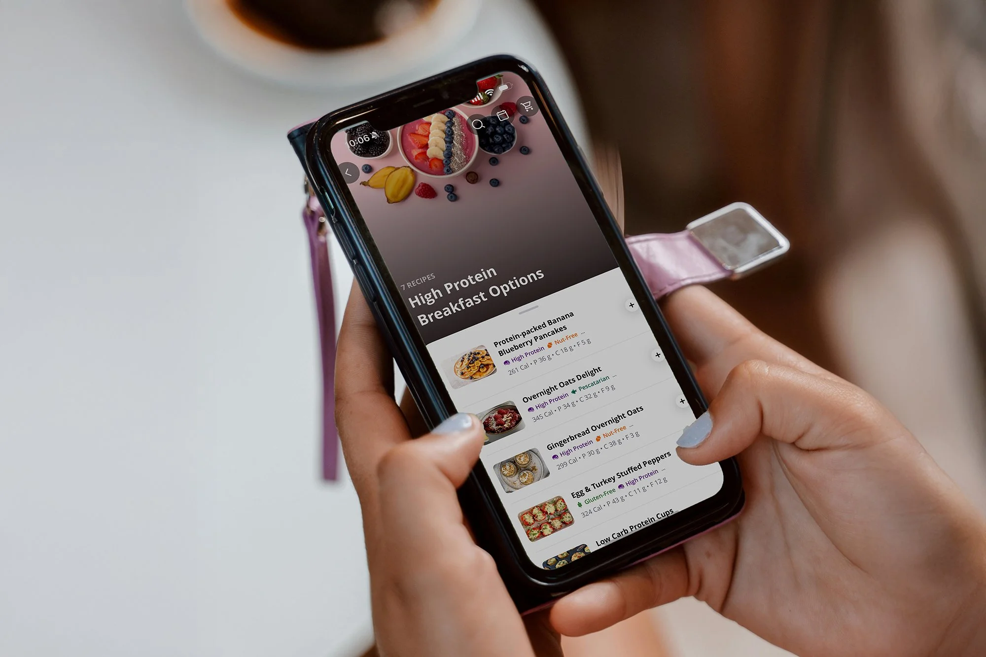 Person holding a smartphone displaying a meal planning app with high-protein breakfast options, including pancakes, oats, and egg dishes.