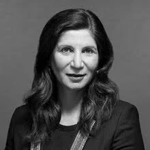 A grayscale portrait of a woman with long wavy dark hair, wearing a dark blazer or top.