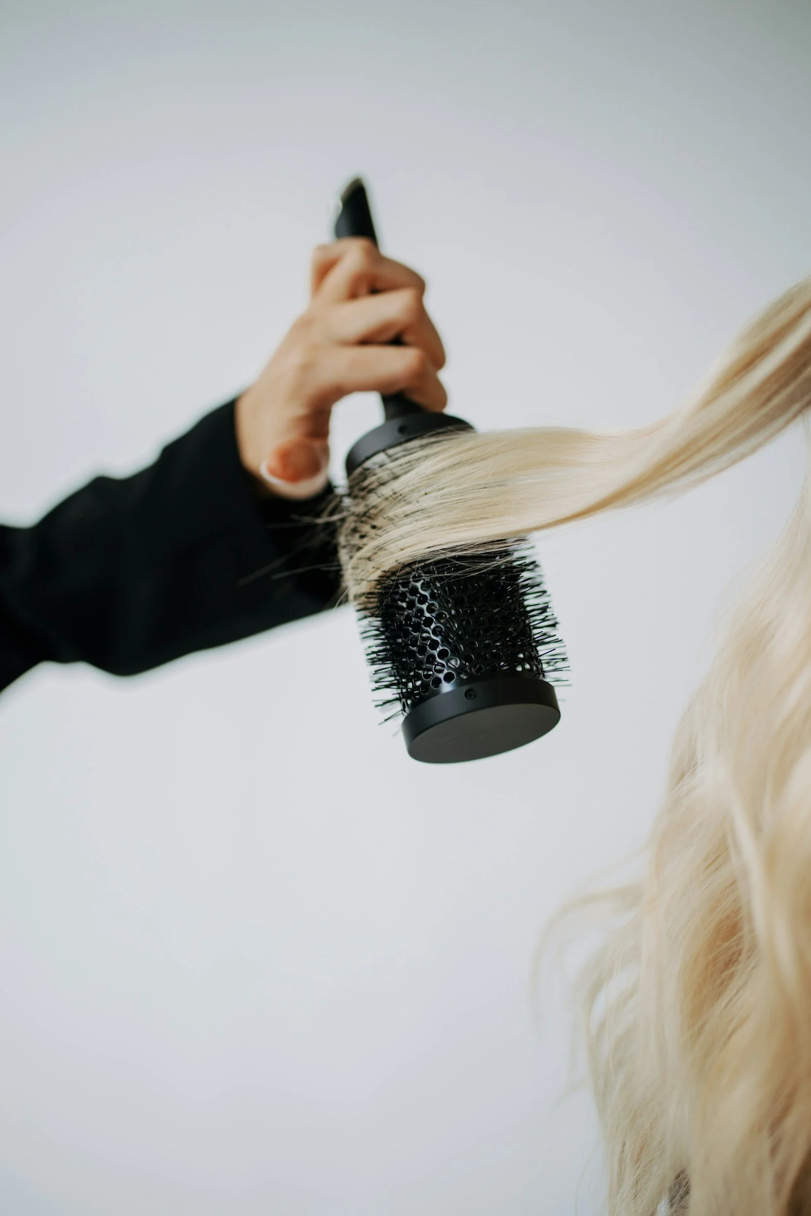 Person using a round hairbrush to style long blonde hair.