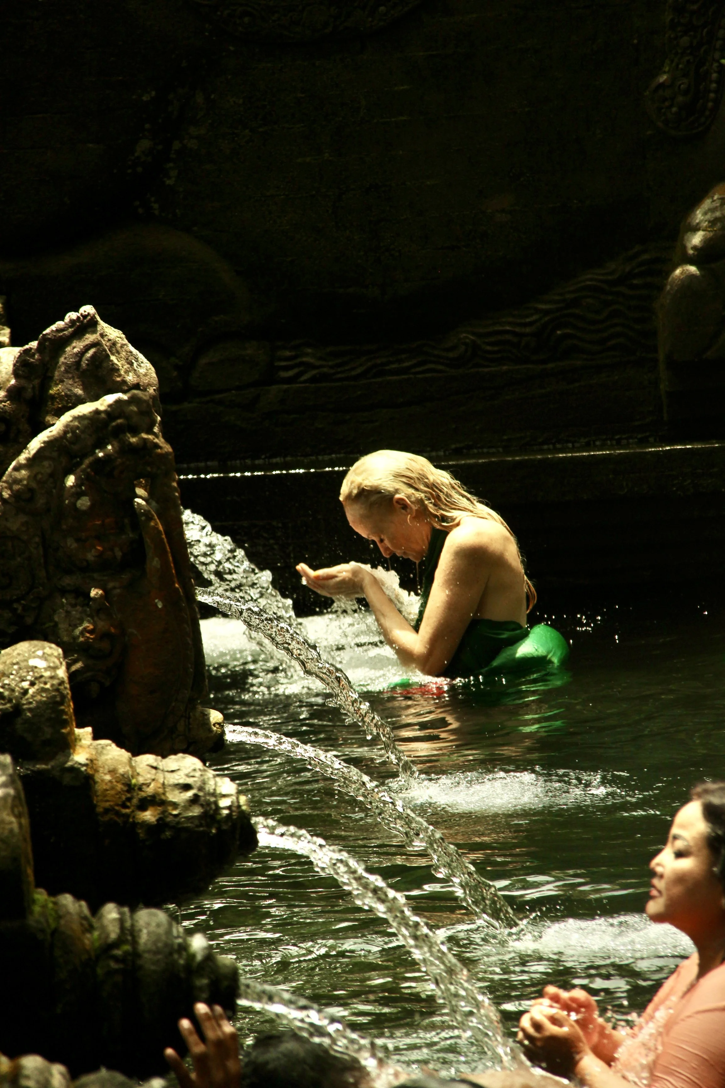 People bathing in a water fountain with carved stone sculptures.
