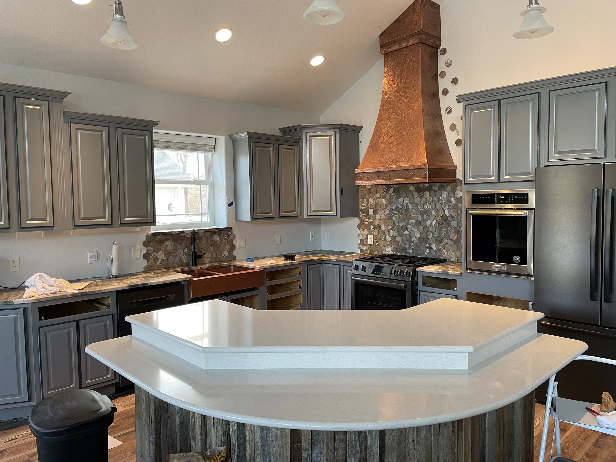 Comprehensive kitchen remodel by Quality Control Painting in Lake Ozark featuring custom grey painted cabinets, a copper vent hood, and professional interior finishing.