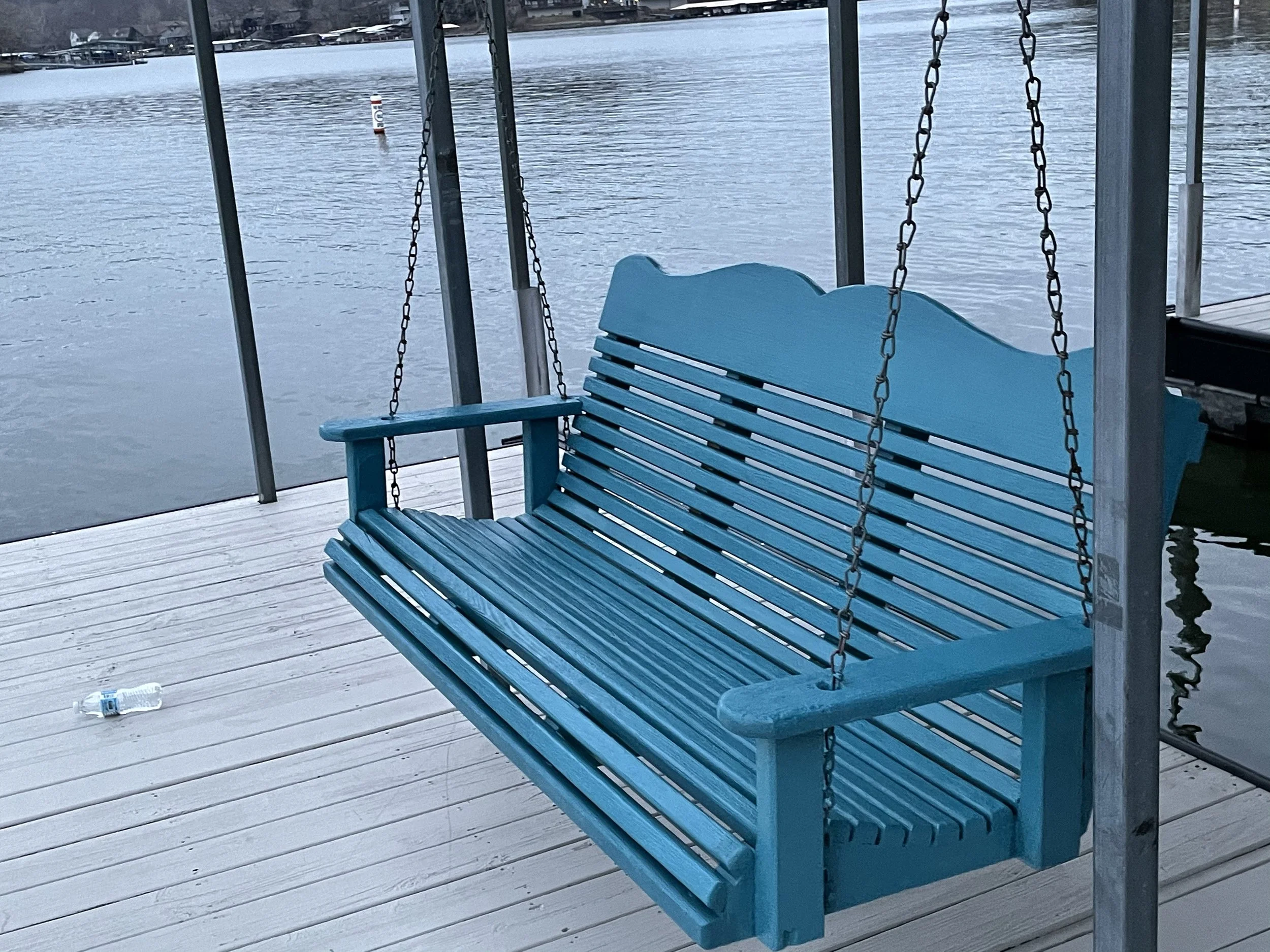 Vibrant blue painted wooden dock swing hanging over a lakefront dock, a custom exterior project by Quality Control Painting.
