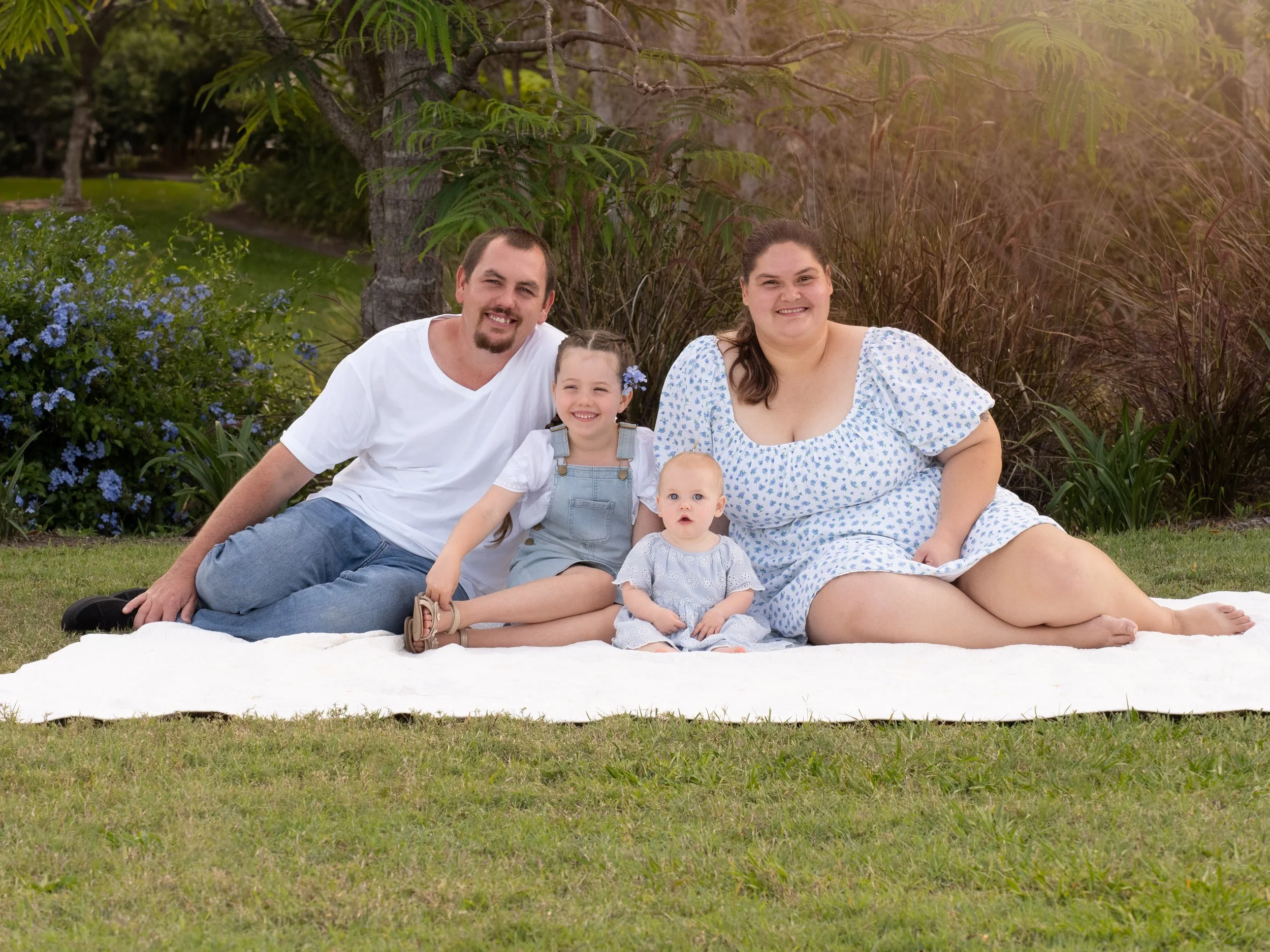 A family of four smiling and hugging outdoors in a park on a sunny day.