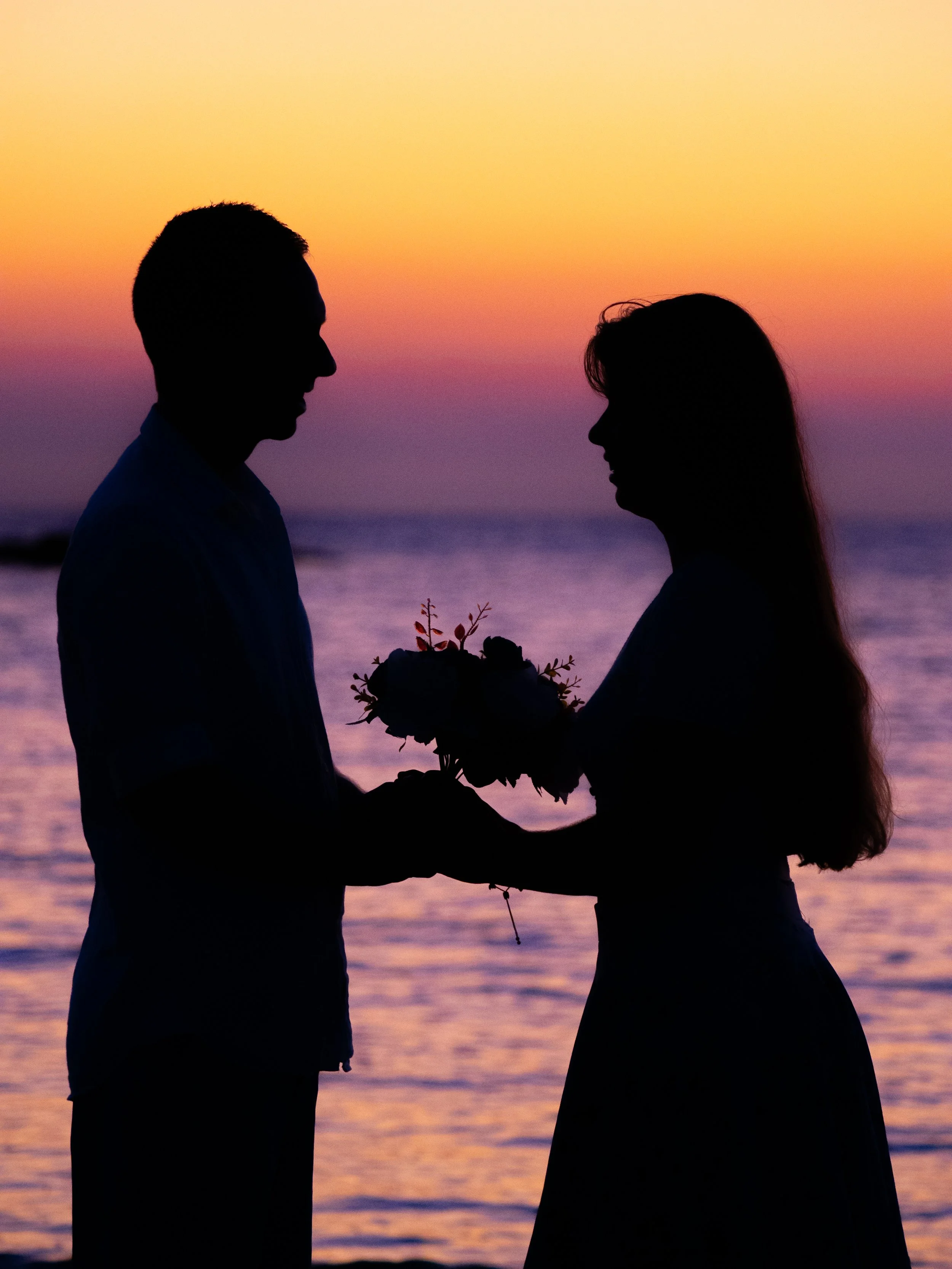 SIlhouette of a man giving a woman a bouquet of flowers at the beach at sunrise