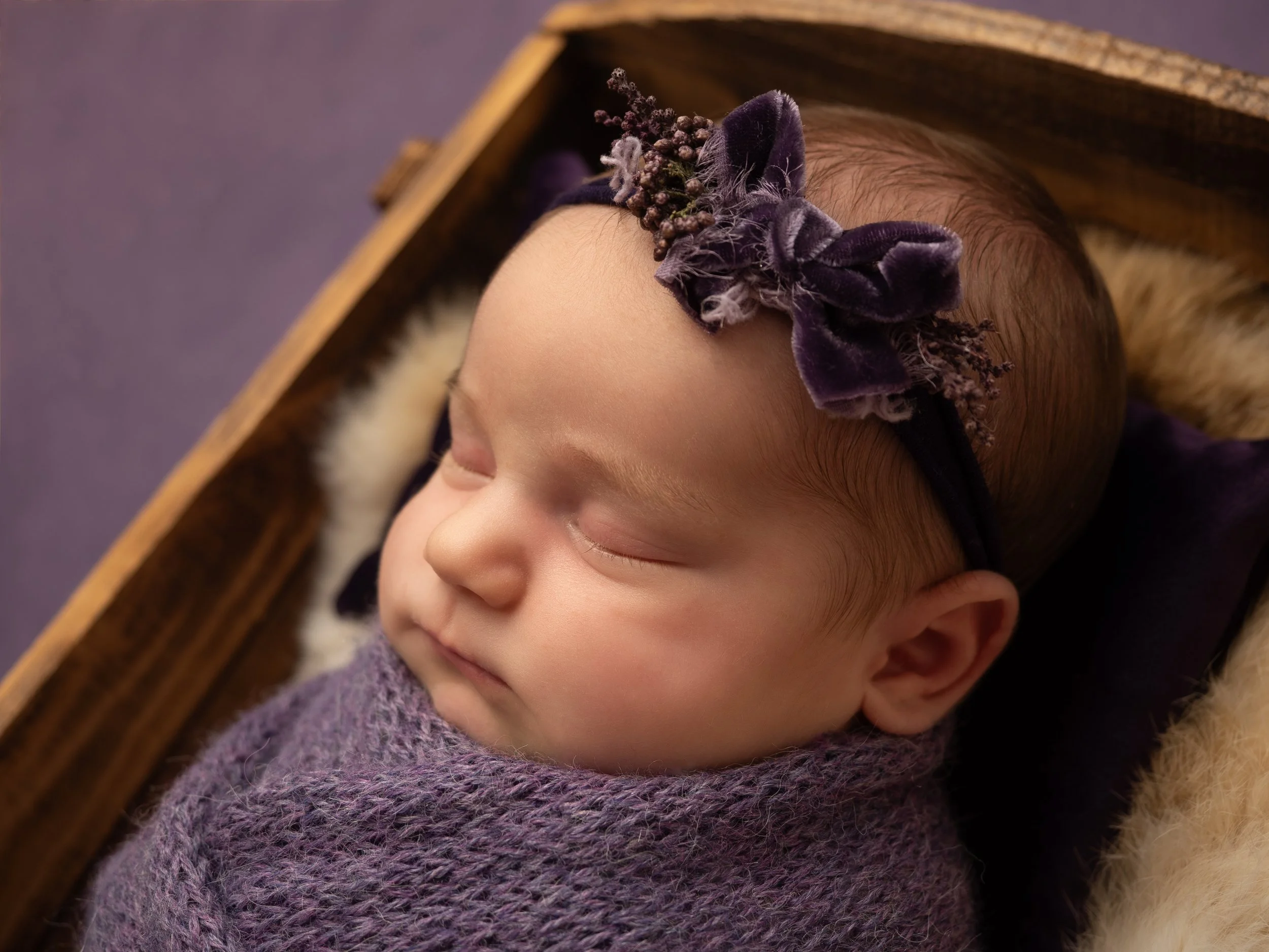 Baby in a crib with a soft knitted purple wrap and velvet purple bow headband