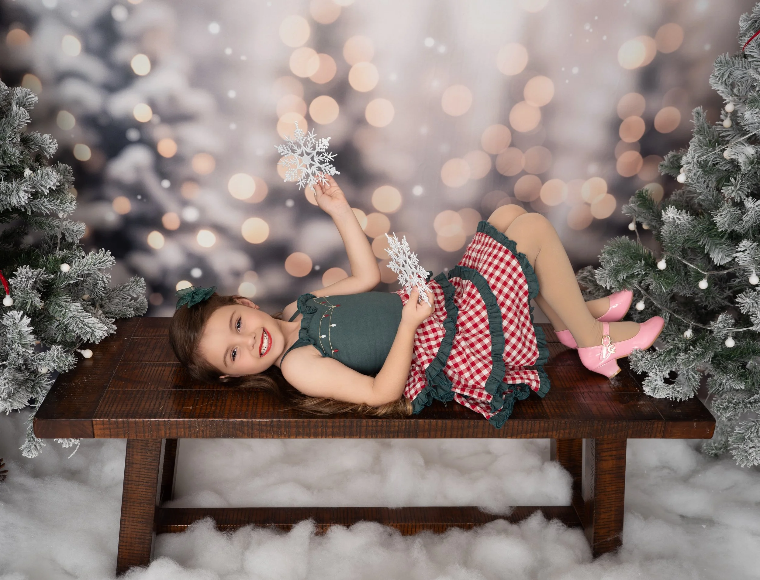Young girl lying on a rustic wooden bench and playing with snowflakes during a Christmas mini session