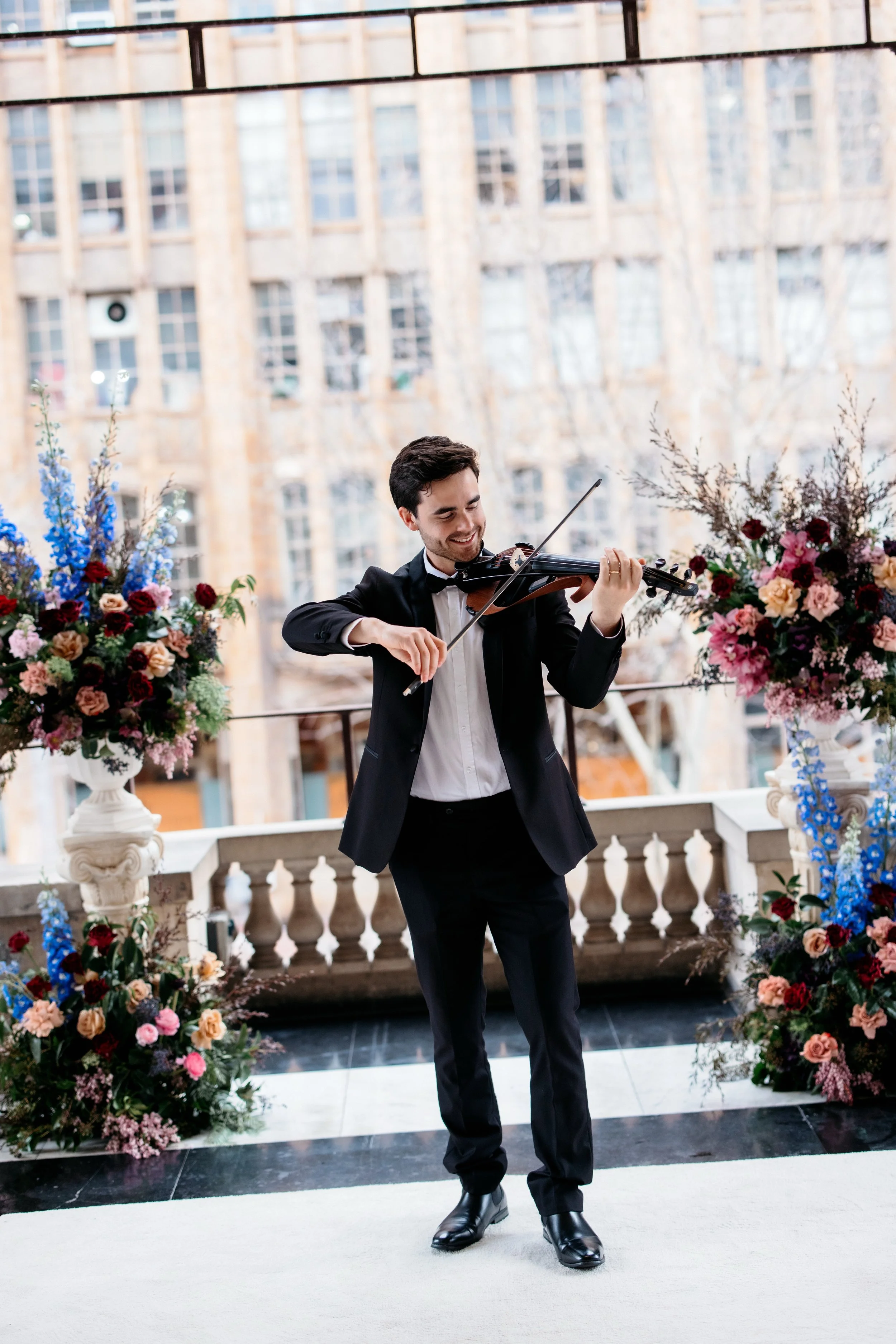 A man in a tuxedo playing a violin at a wedding, with a cityscape in the background.