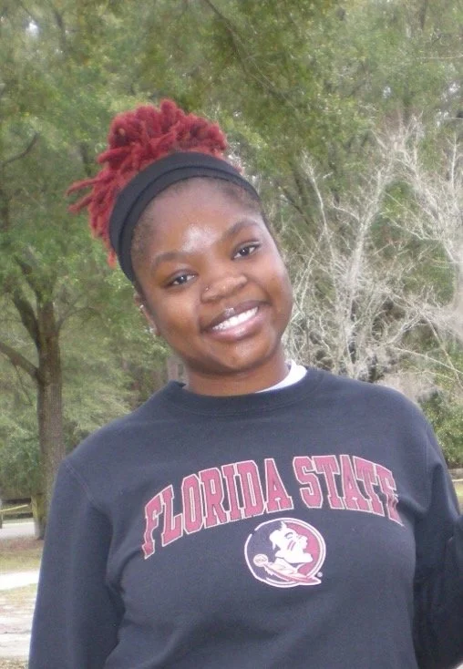 Young woman outdoors wearing a black Florida State sweatshirt and a black headband with red dreadlocks tied up.