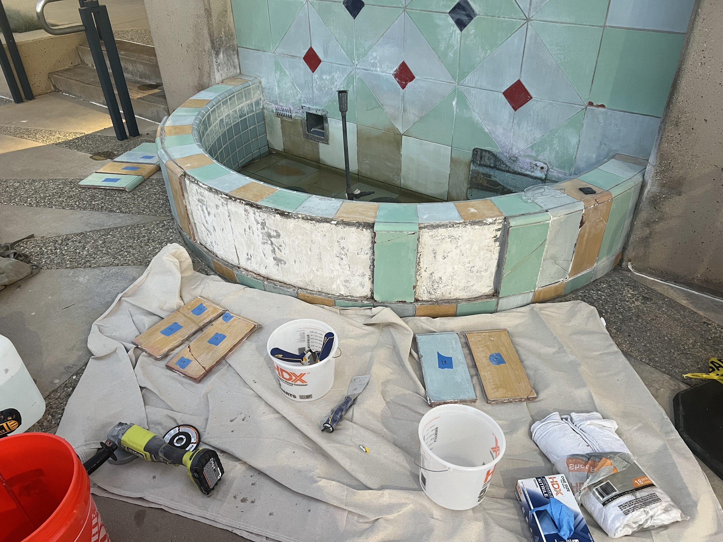 Many tile laying tools are set out on a drop cloth. Color matched grout is being tested in samples and detached tiles are labeled.