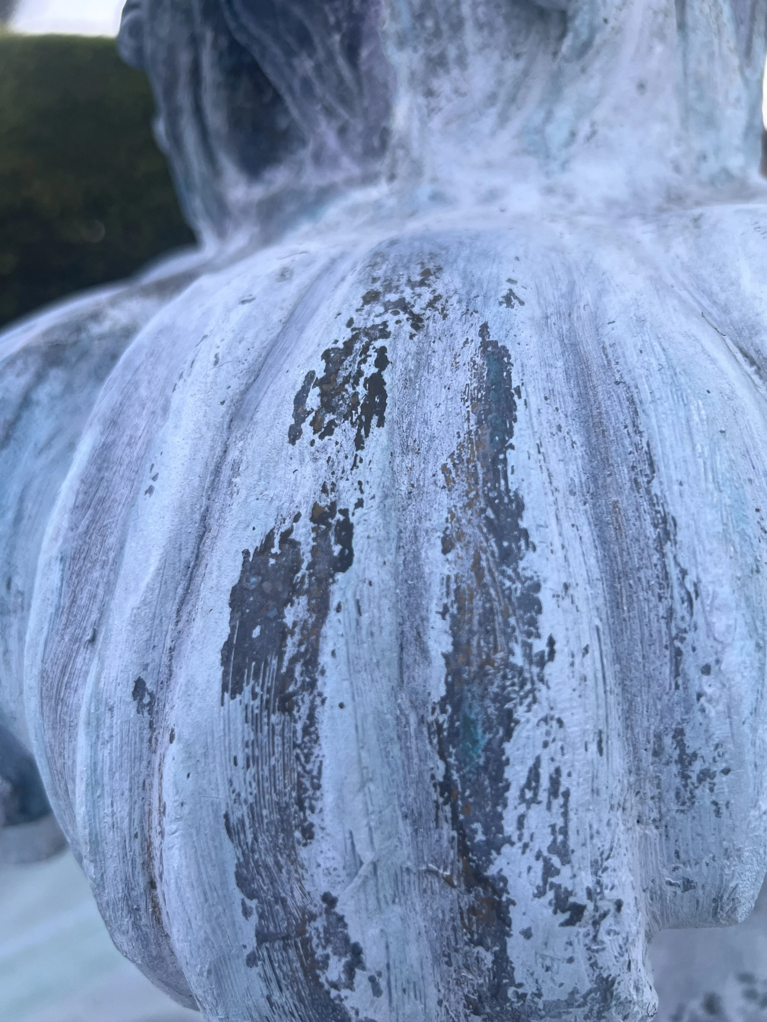 Close-up of a weathered, metallic sculpture with peeling paint and rust, with water flowing over it.