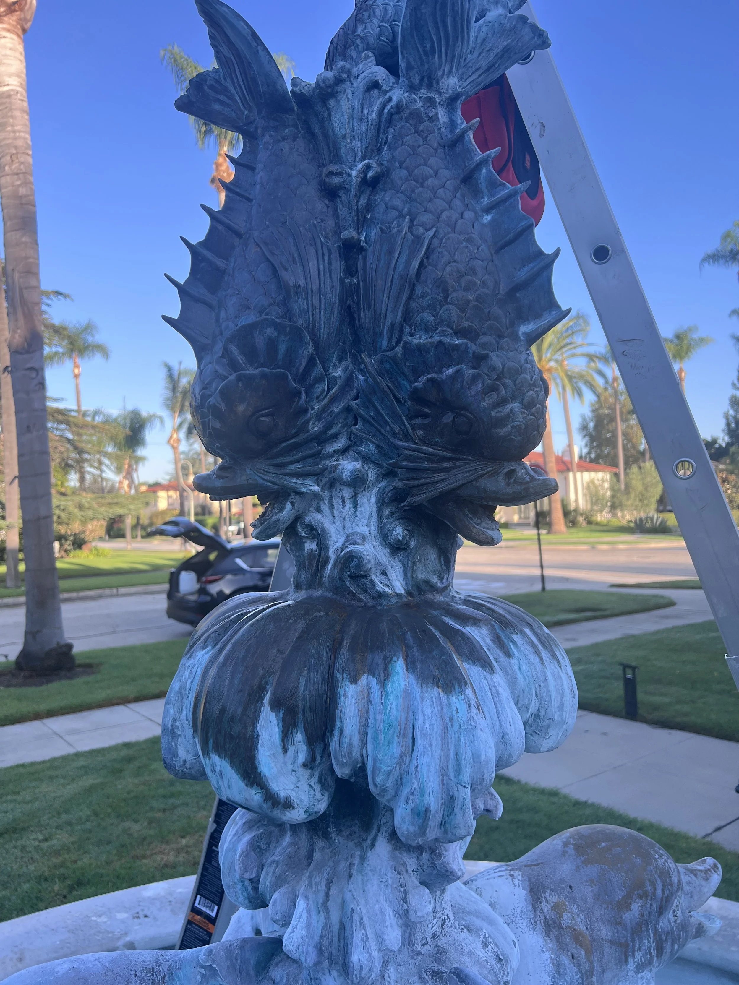 A detailed stone sculpture of a seahorse with a large fin on its back, surrounded by coral-like features, situated outdoors with palm trees and a clear blue sky in the background.
