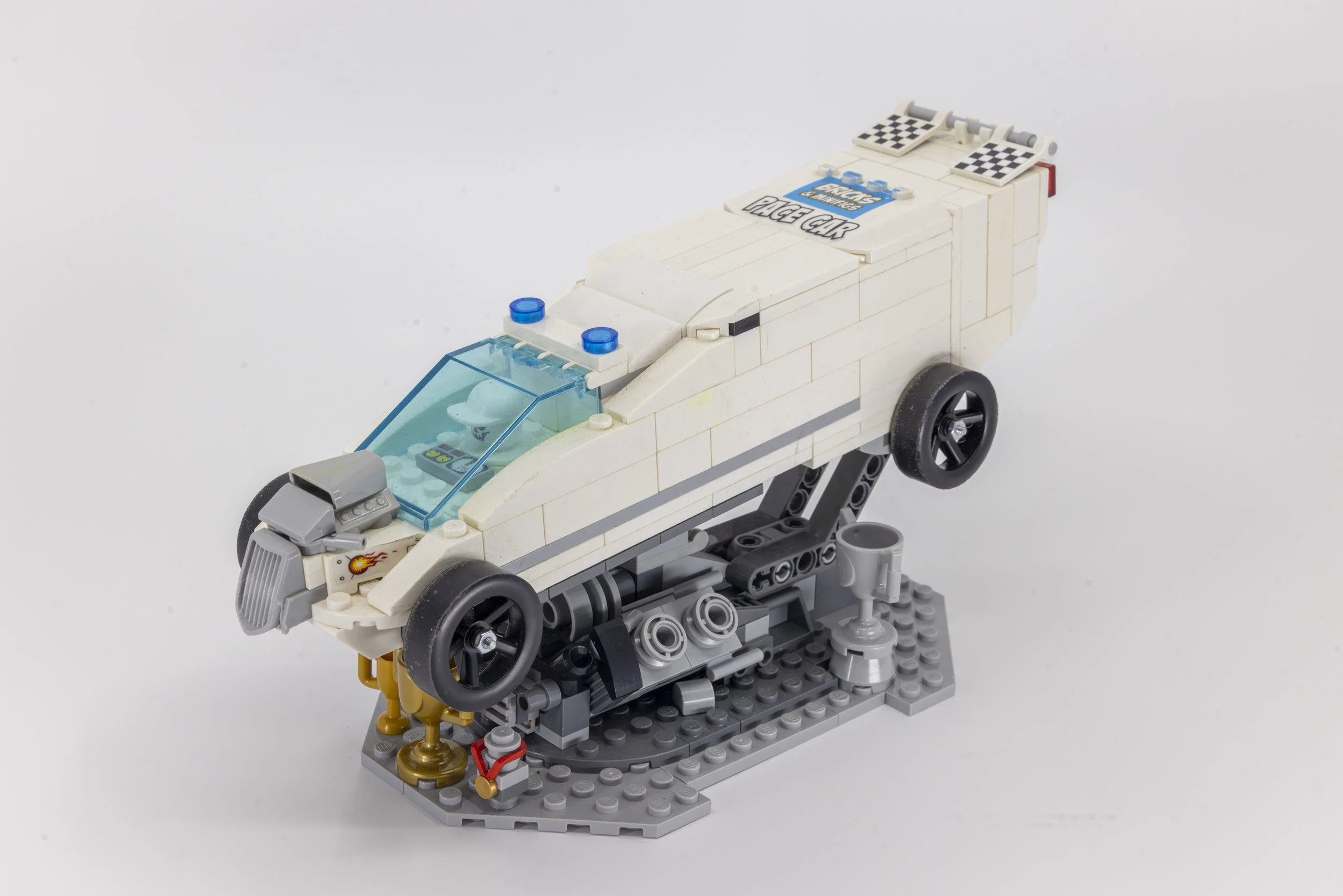 LEGO model of a white race car with checkered flags on the back, black wheels, a blue-tinted windshield, and a small driver figure inside.