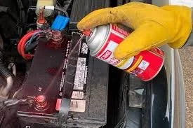 Person wearing yellow gloves holding a spray can near a car battery.
