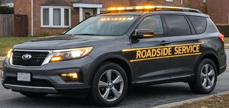 Black roadside service vehicle with yellow lettering and flashing lights on the roof, parked on a residential street in front of a house.