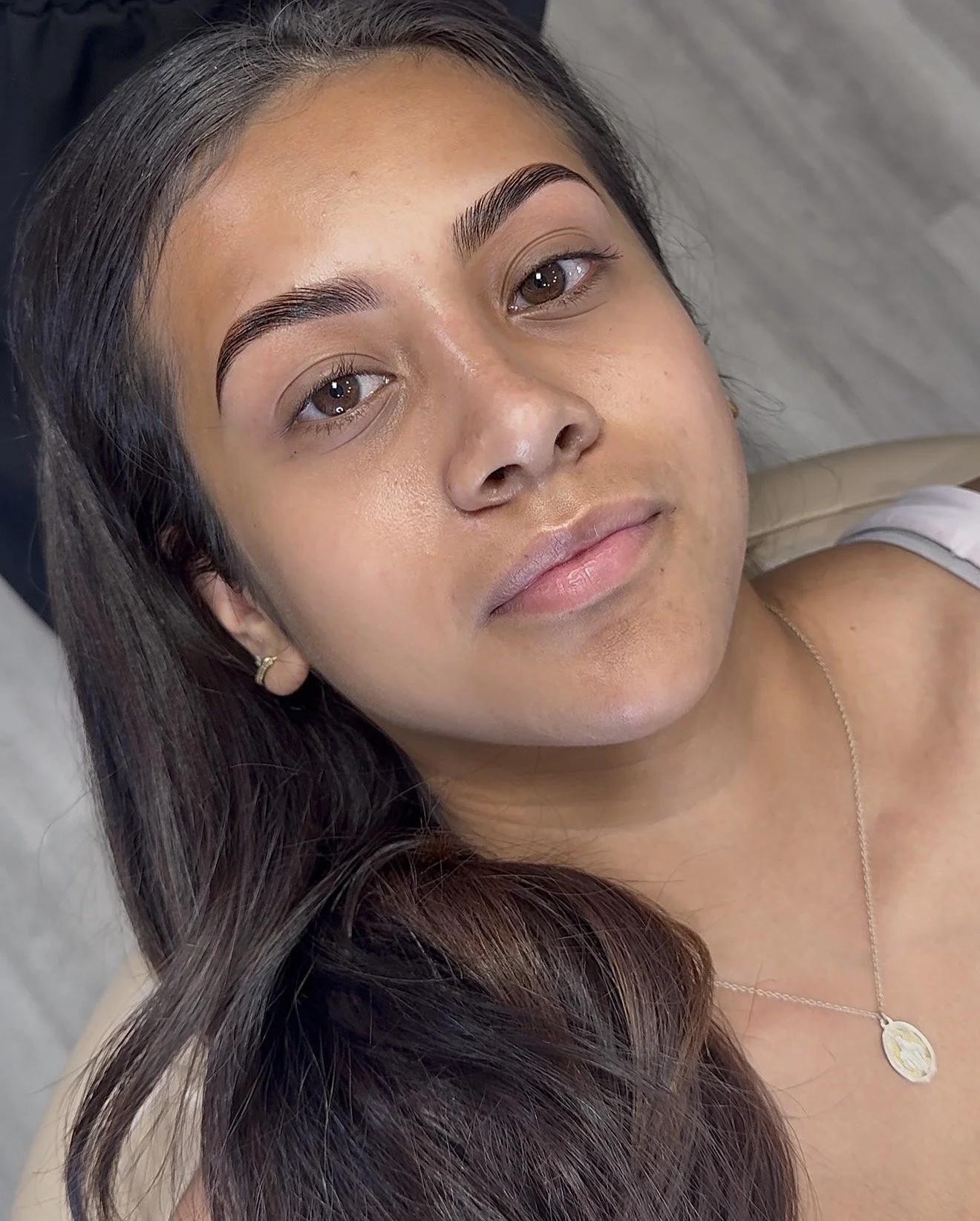 A young woman with long dark hair, brown eyes, and well-groomed eyebrows, looking at the camera with a neutral expression.