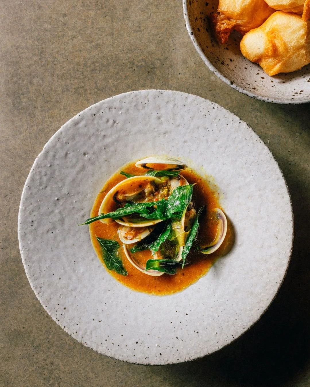 Pippies rest on a grilled slab of heirloom tomato in a fragrant pool of tomato rasam broth, with light, fluffy lentil doughnuts (vadai) to mop it all up. Finished with a scattering of perfectly crisp, savoury curry leaves. A special one for New Year&