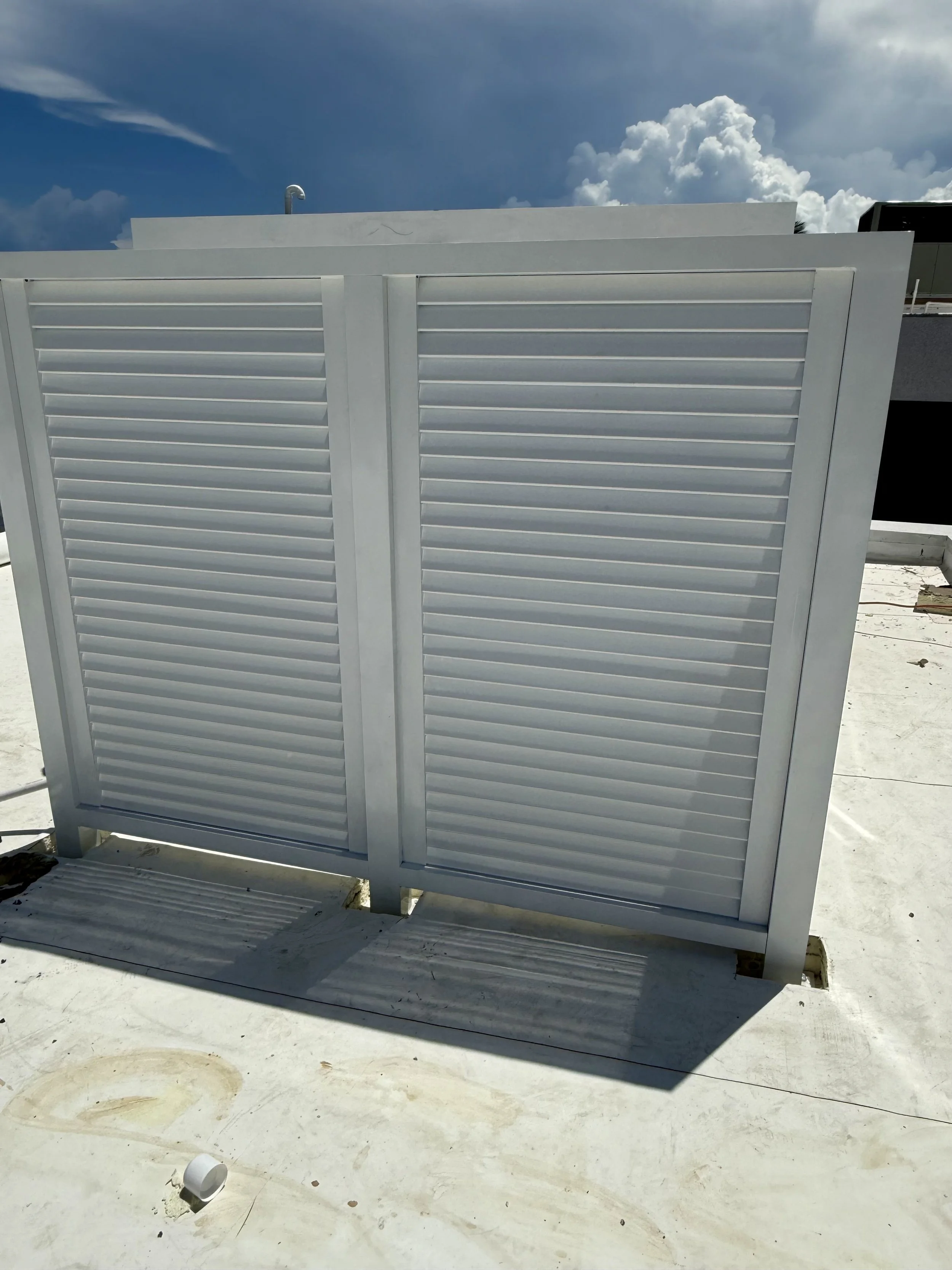 Una vista de una estructura blanca con persianas cerradas en un espacio exterior, con un cielo nublado al fondo, y algunos objetos sobre una superficie de concreto.