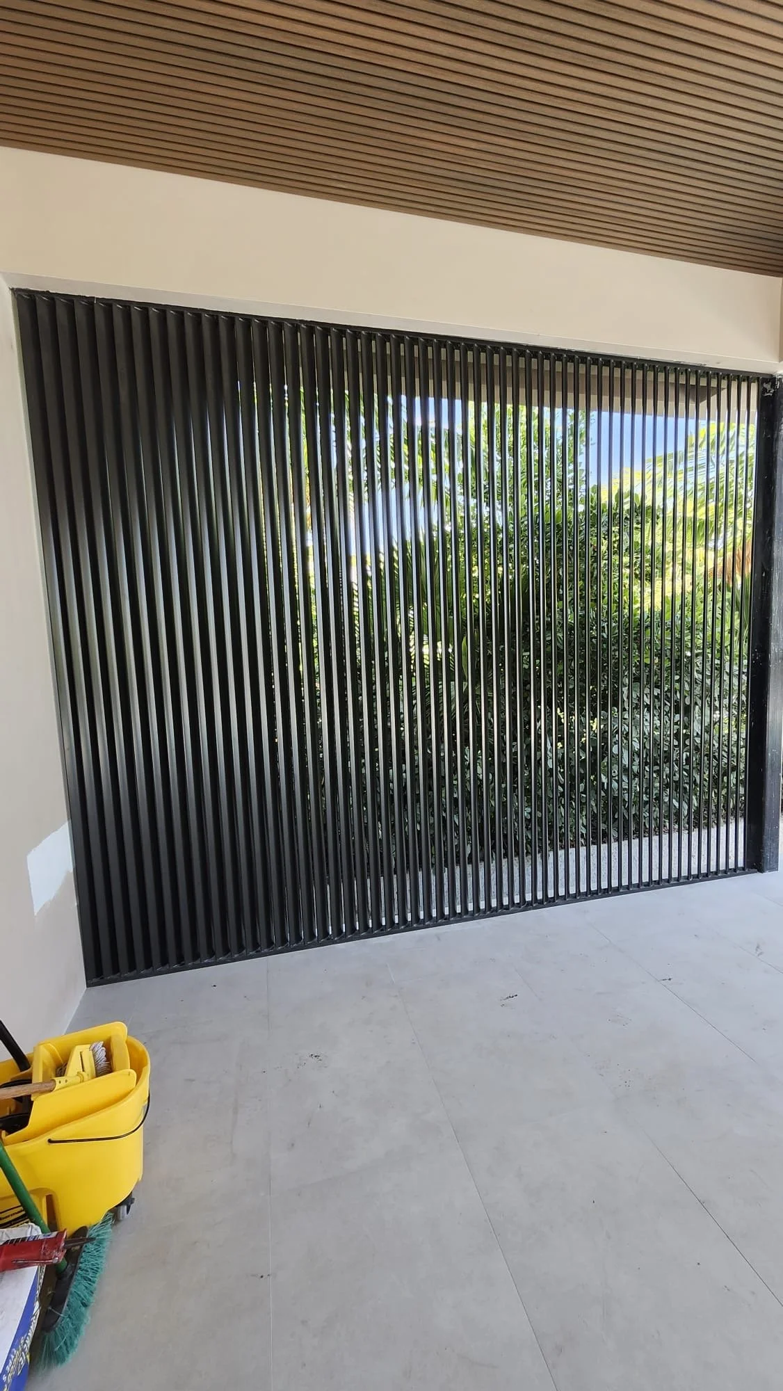 Reja negra con diseño de barras verticales, ventana con vista a vegetación exterior.