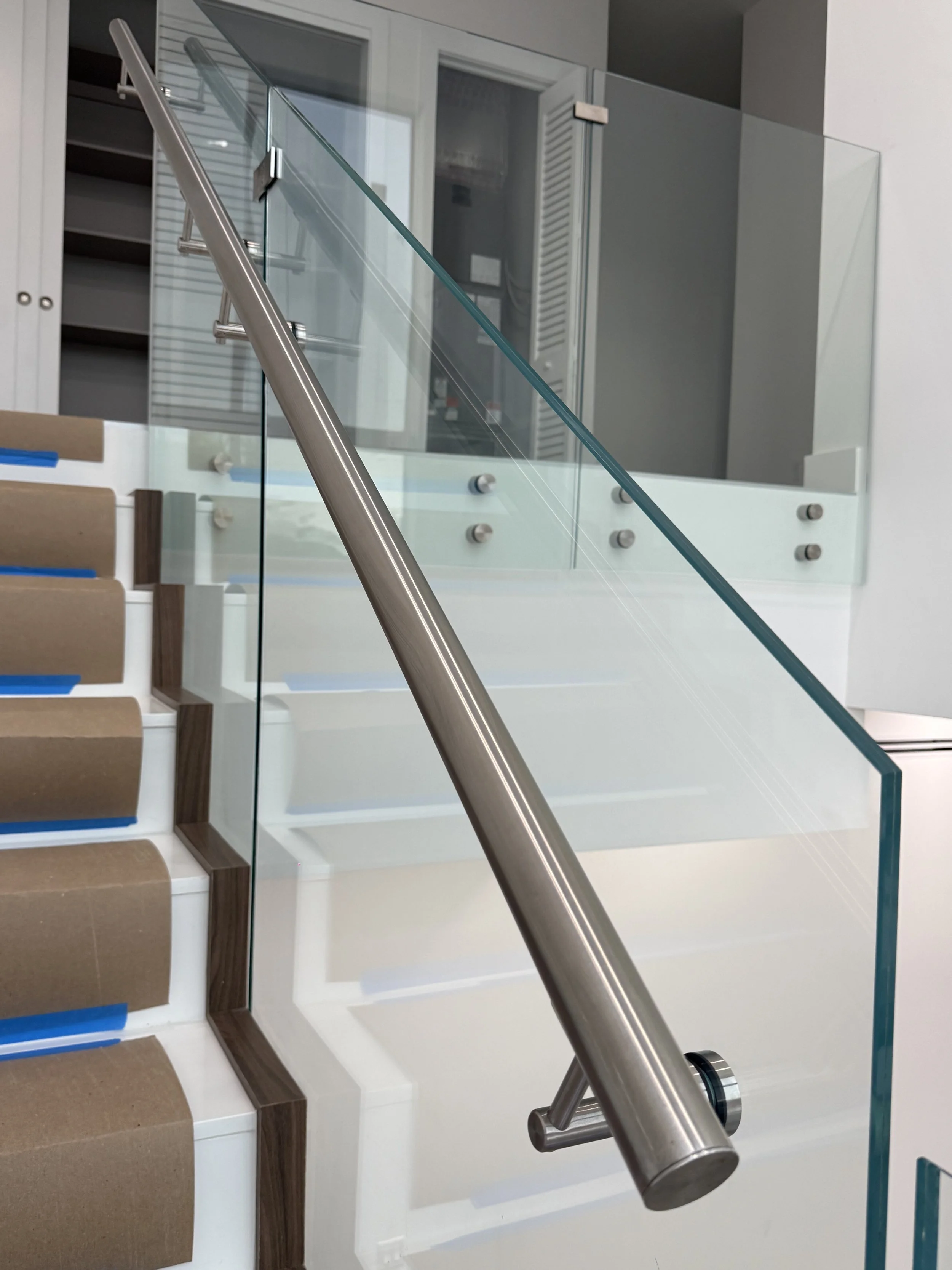 Escalera moderna con barandilla de metal y barandilla de vidrio, en un interior con paredes blancas y armarios. El ángulo de la foto está invertido.