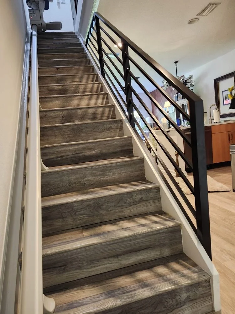 Escalera de madera con barandilla negra en interior de casa, vista desde abajo hacia arriba.