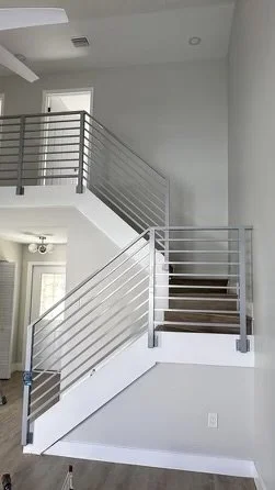 Escalera interior de dos niveles con barandales metálicos blancos y paredes blancas, en una casa moderna.