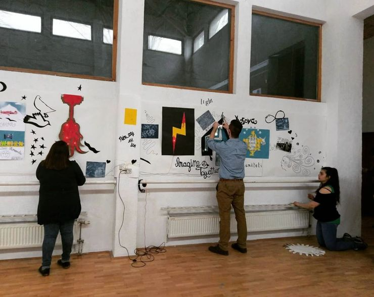 Three people creating a colorful mural on a white wall in an indoor space with wooden floors.
