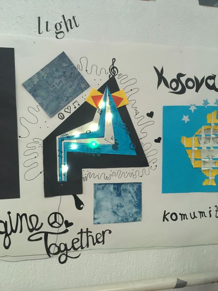 A colorful, abstract art piece on a poster with murals of a star, musical notes, peace signs, and handwritten words like 'light,' 'together,' and 'komunizt' in black marker. The star is illuminated with small LED lights.