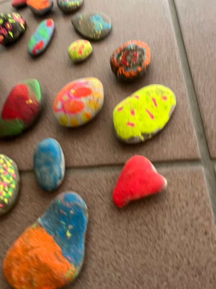 Colored rocks painted with bright, varied designs, arranged on a tiled surface.