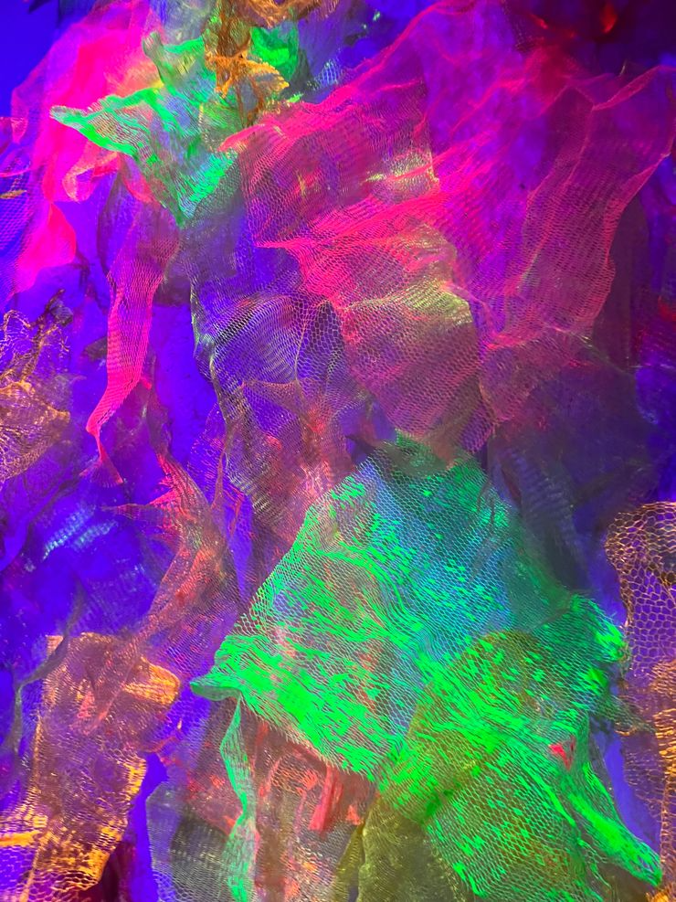 Abstract colorful, iridescent fabric with neon hues of pink, green, purple, and gold, creating a vibrant textured pattern.