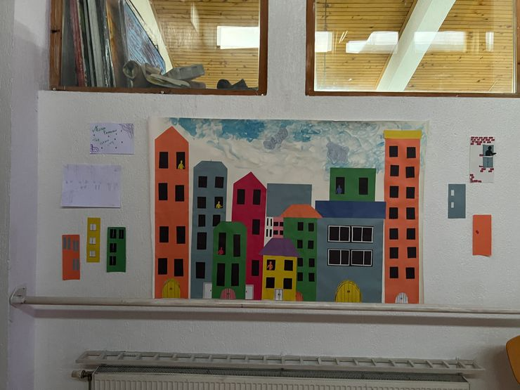 Colorful paper cut-out of a cityscape with various tall and short buildings on a wall.