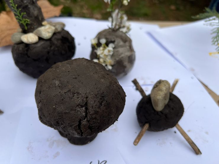 Small art project with rocks and soil arranged on paper, some decorated with small stones and plant material.