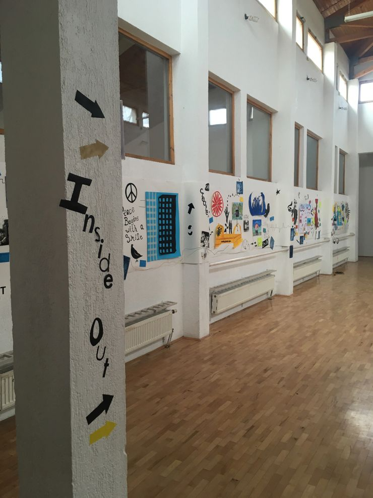 Interior of a room with white walls and a wooden floor, decorated with colorful artwork and signs, including a vertical sign on a corner pillar that says 'Inside Out' with arrows pointing in different directions.