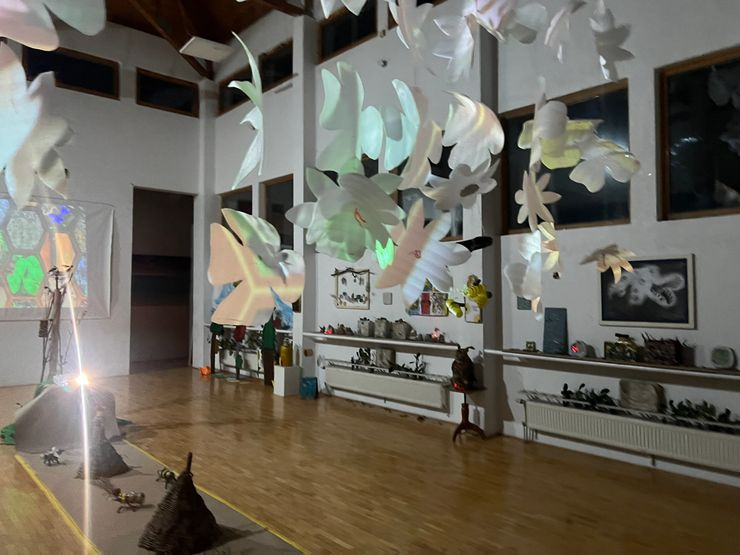 Indoor art installation with hanging paper flowers or butterflies, soft lighting, and shelves with various decorative items in a spacious room.
