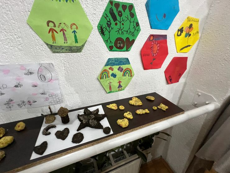 Colorful drawings on green, blue, yellow, and red paper hang on a white wall above a table with rocks and yellow popcorn.