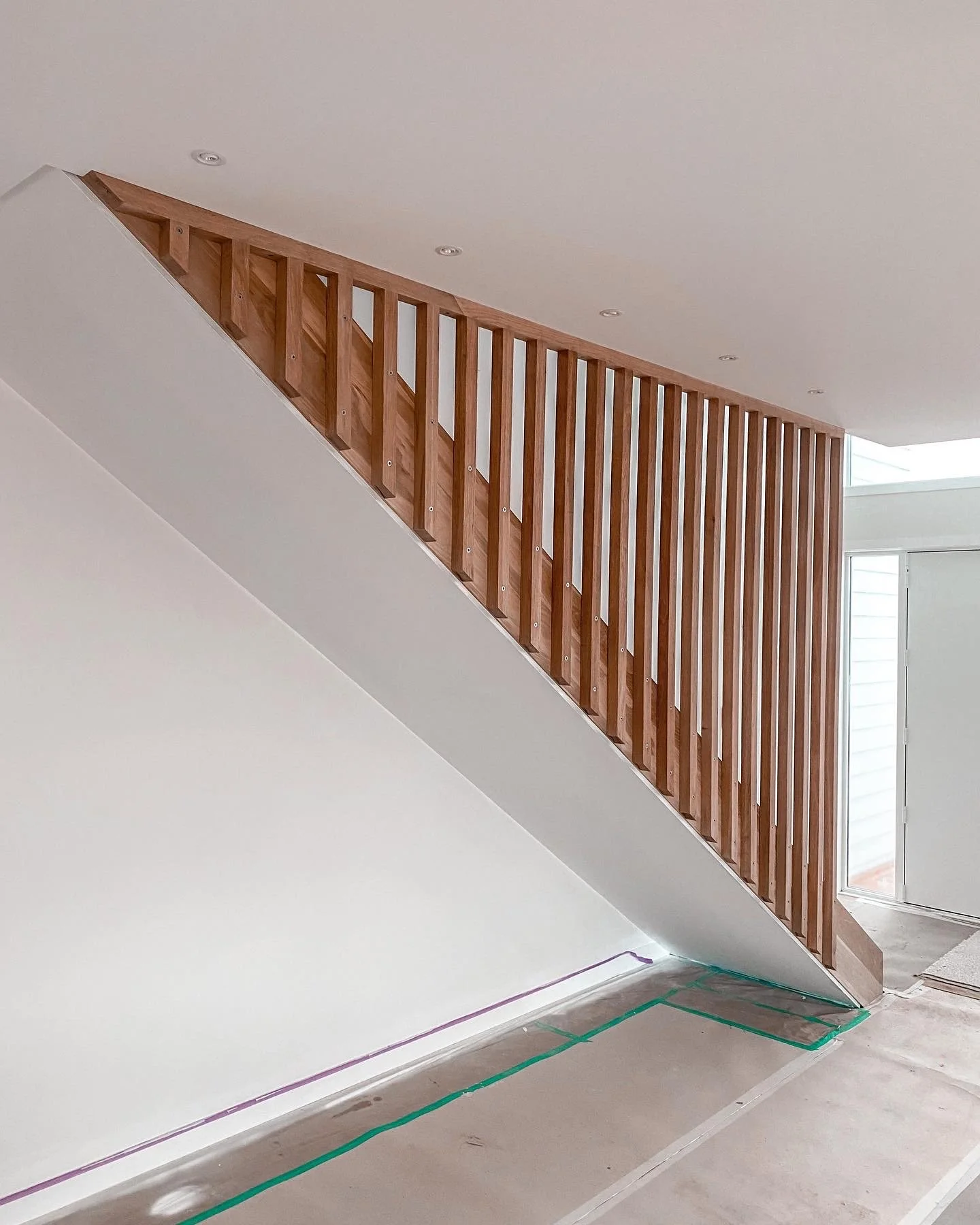 Interior view of a staircase with a wooden railing and new paint on the wall, with construction tape on the floor.