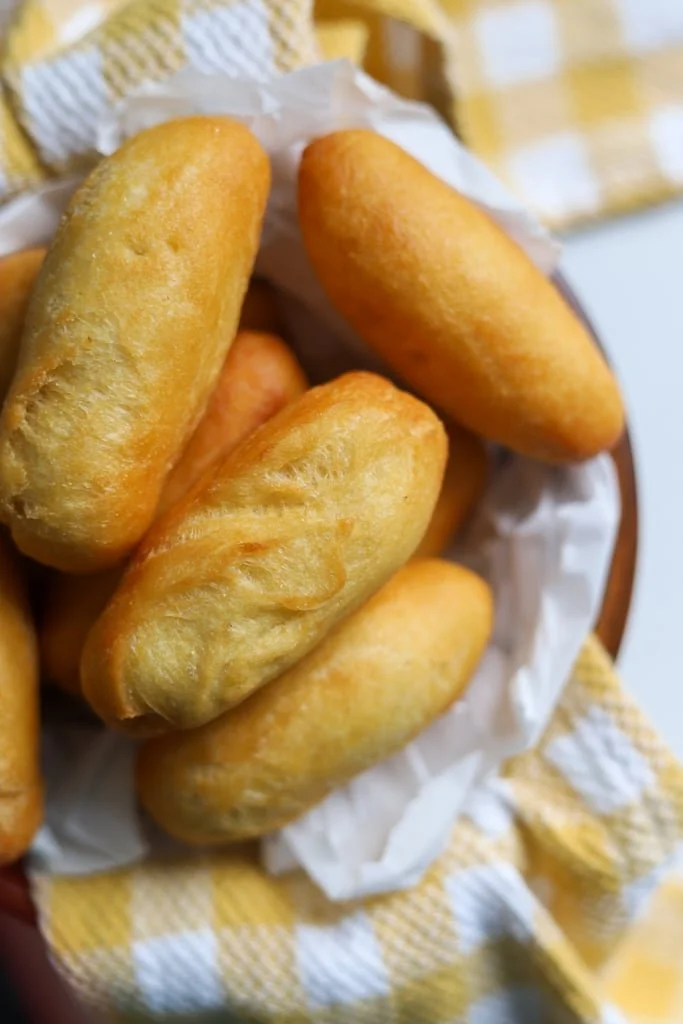 Golden-brown fried mozzarella sticks in a basket lined with paper, with a yellow and white checkered cloth underneath.