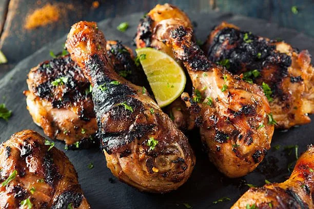 Grilled chicken drumsticks topped with herbs and sauce, garnished with lime wedges and chopped green herbs, on a dark serving plate.