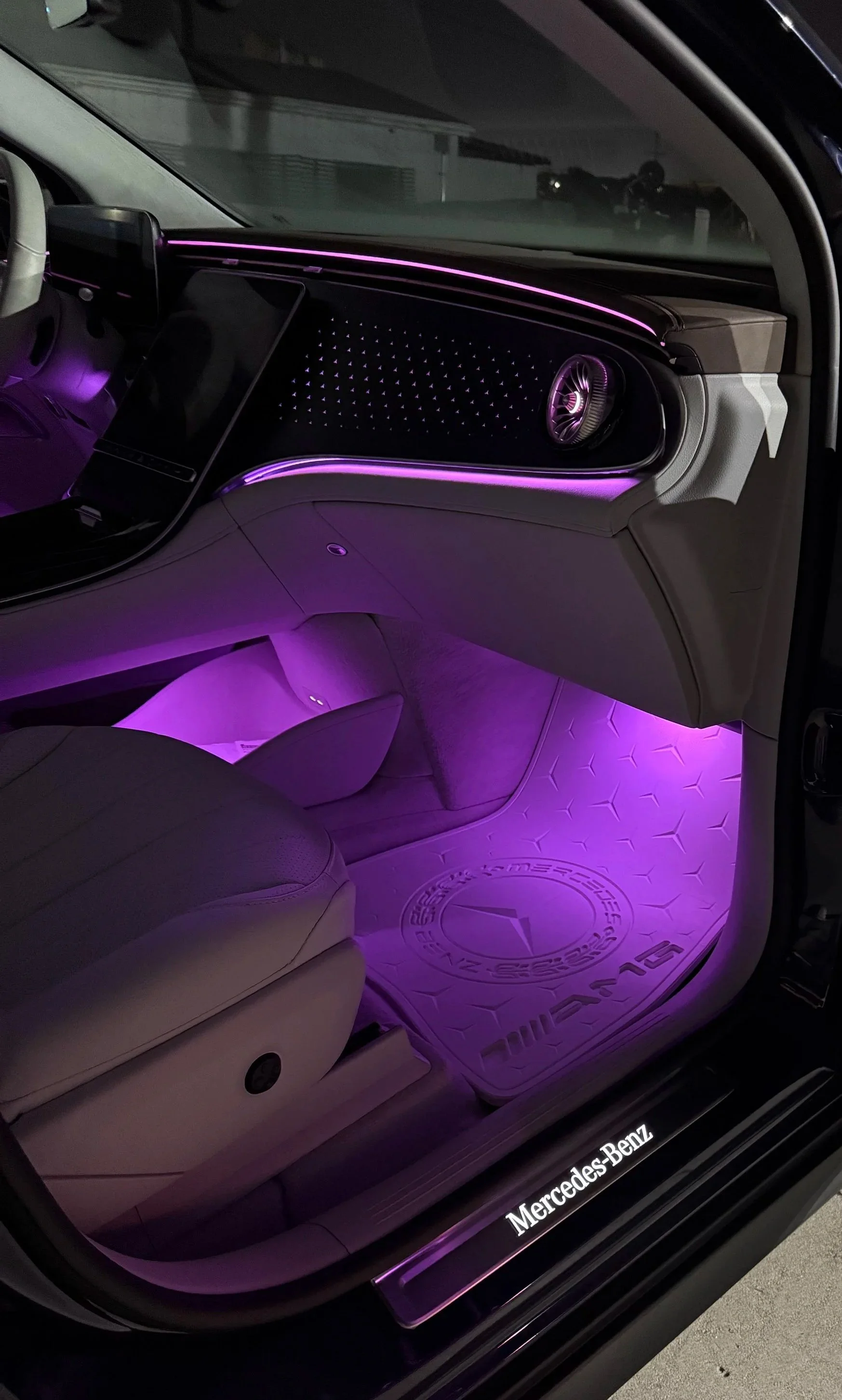The interior of a Mercedes-Benz vehicle illuminated with purple ambient lighting, showing the dashboard, a digital display, and an exclusive AutoFloor custom made for the Mercedes-Benz.