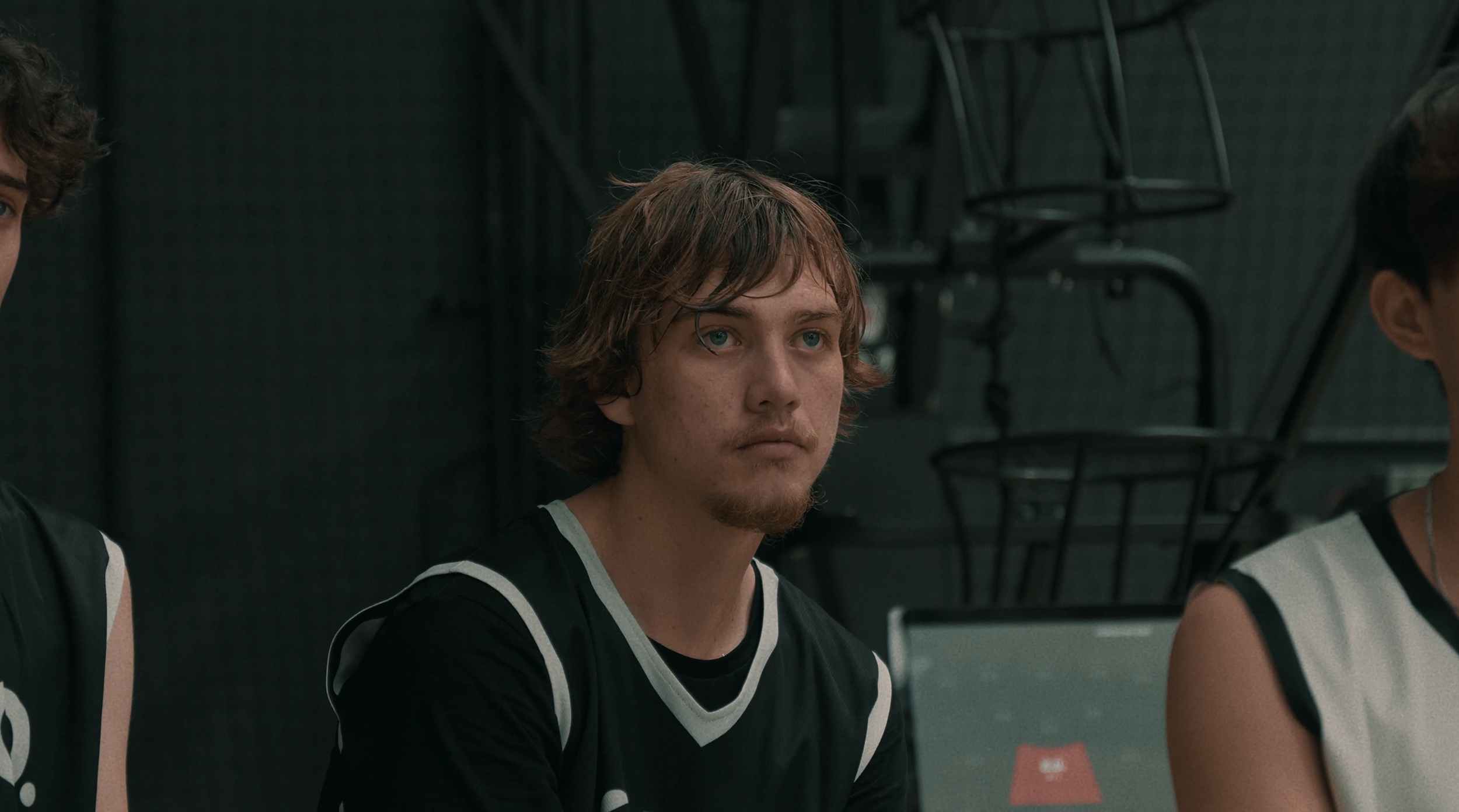 A young male basketball player with blonde hair and blue eyes sitting on the bench during a game.