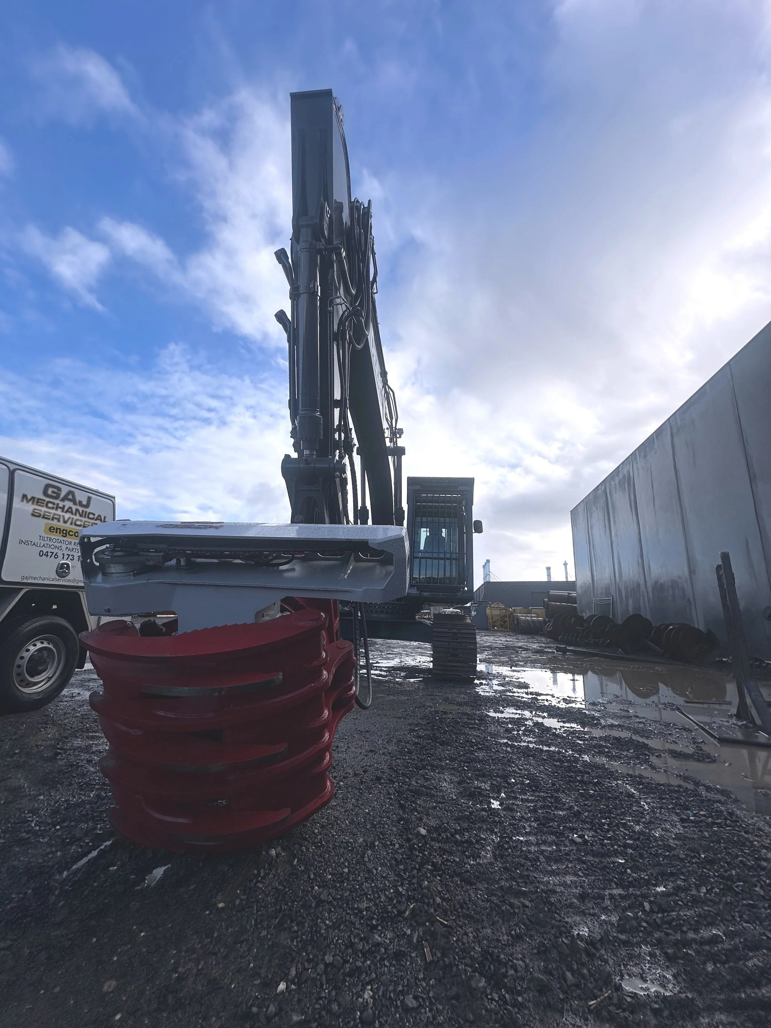Construction excavator on muddy ground with a partly cloudy sky in the background.