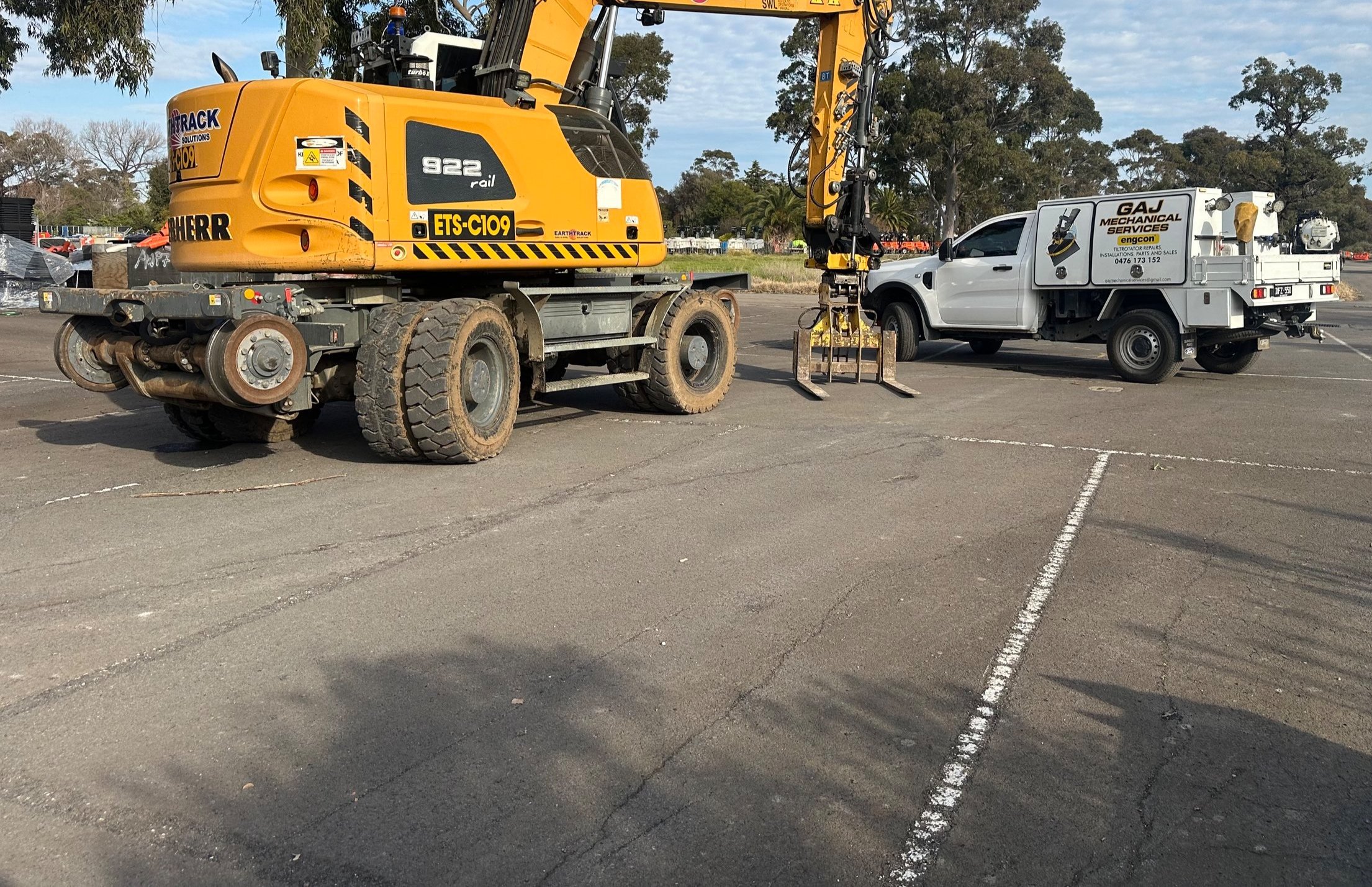 A construction site with a yellow liebherr hi-rail excavator and a white utility truck parked in a lot.