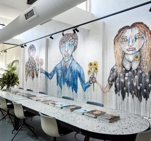 A 10m long conference table with chairs, in front of a wall featuring colourful murals of three stylized women holding flowers.