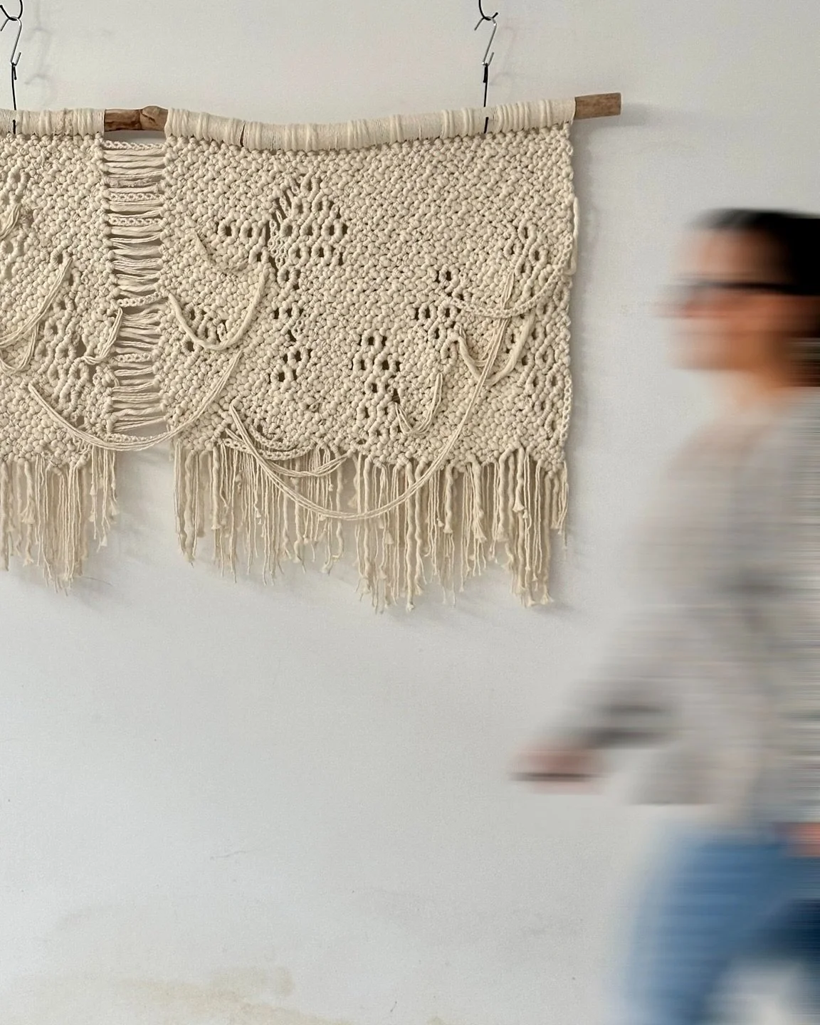 A large scale macrame wall hanging made of natural cotton, featuring intricate macrame patterns and fringes, mounted on a natural branch against a white wall | Ana Salazar Atelier