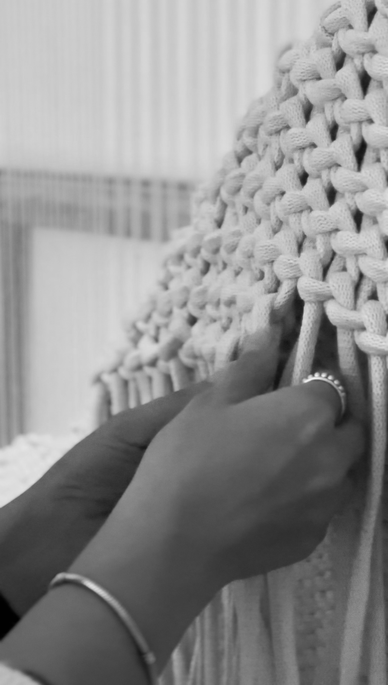 A person's hand weaving or working on a large, textured, woven art piece using thick, string-like material.