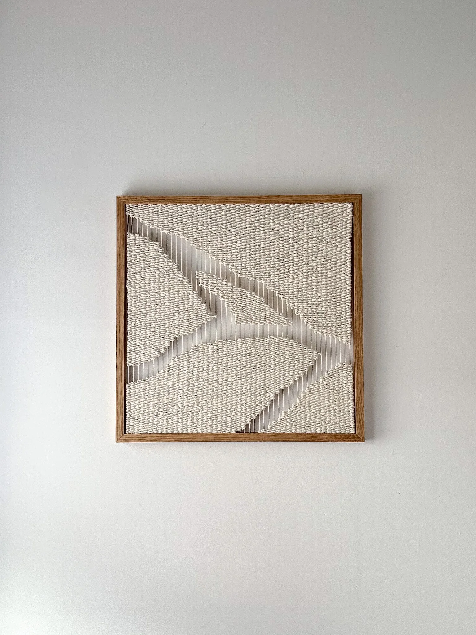 Decorative framed textile art featuring abstract leaf patterns on a white wall.