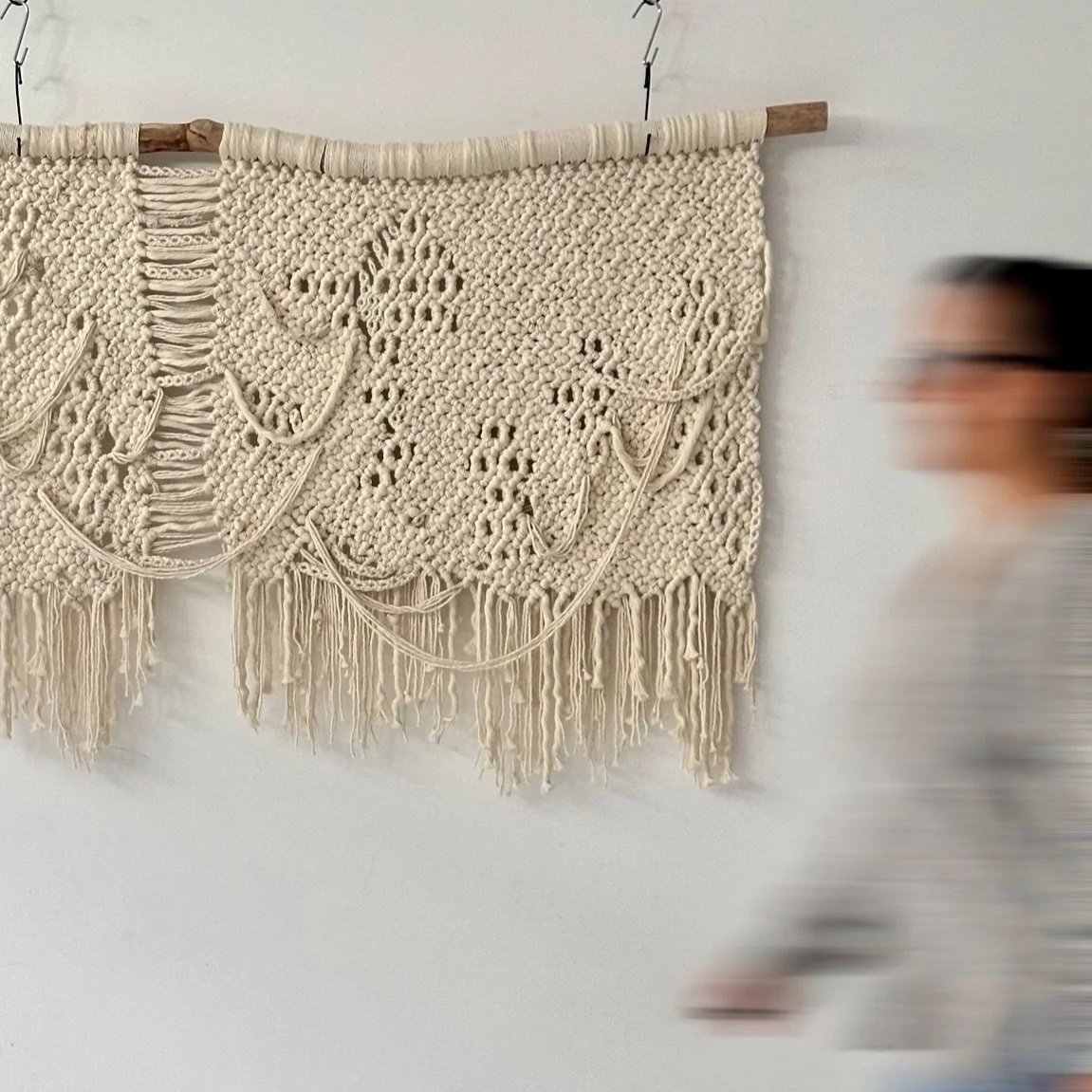 Macrame wall hanging art made of off-white cords with intricate patterns and fringe at the bottom, hanging on a white wall  | Ana Salazar Atelier
