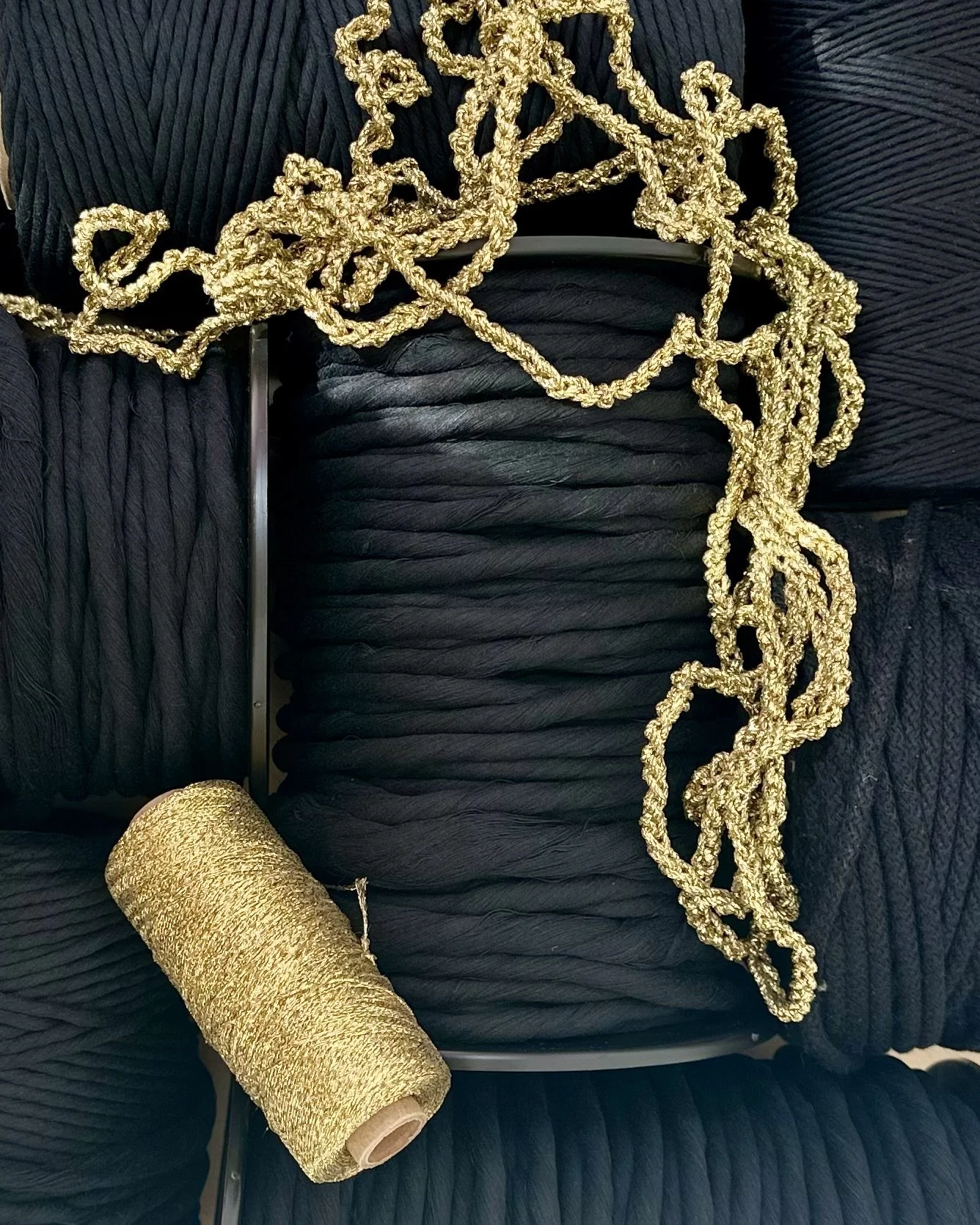 Multiple spools of black thread, a reel of gold thread, and a tangled piece of gold thread | Ana Salazar Atelier fiber curation